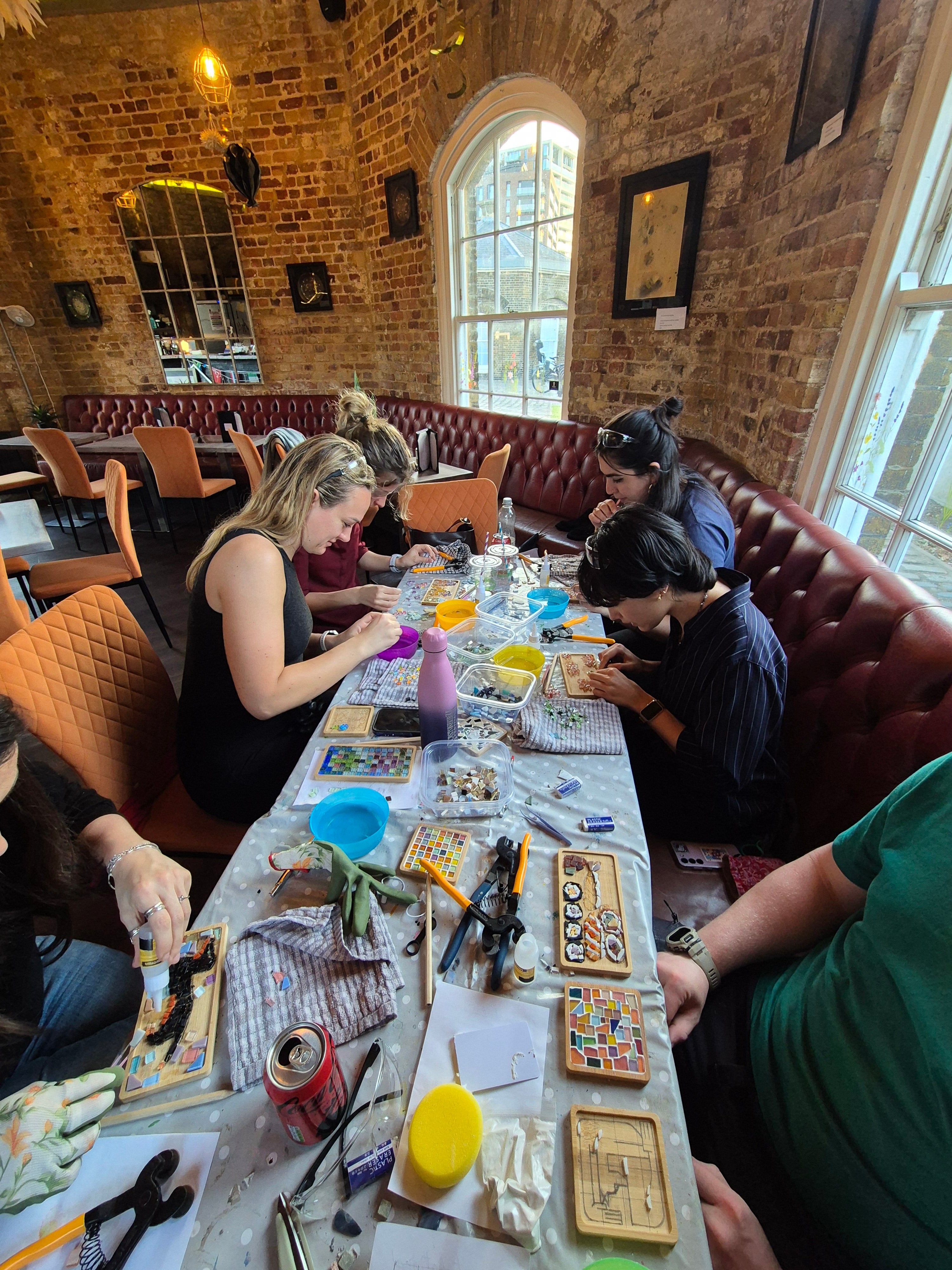 Group of people sitting around a long table in a restaurant, engaged in a craft activity.